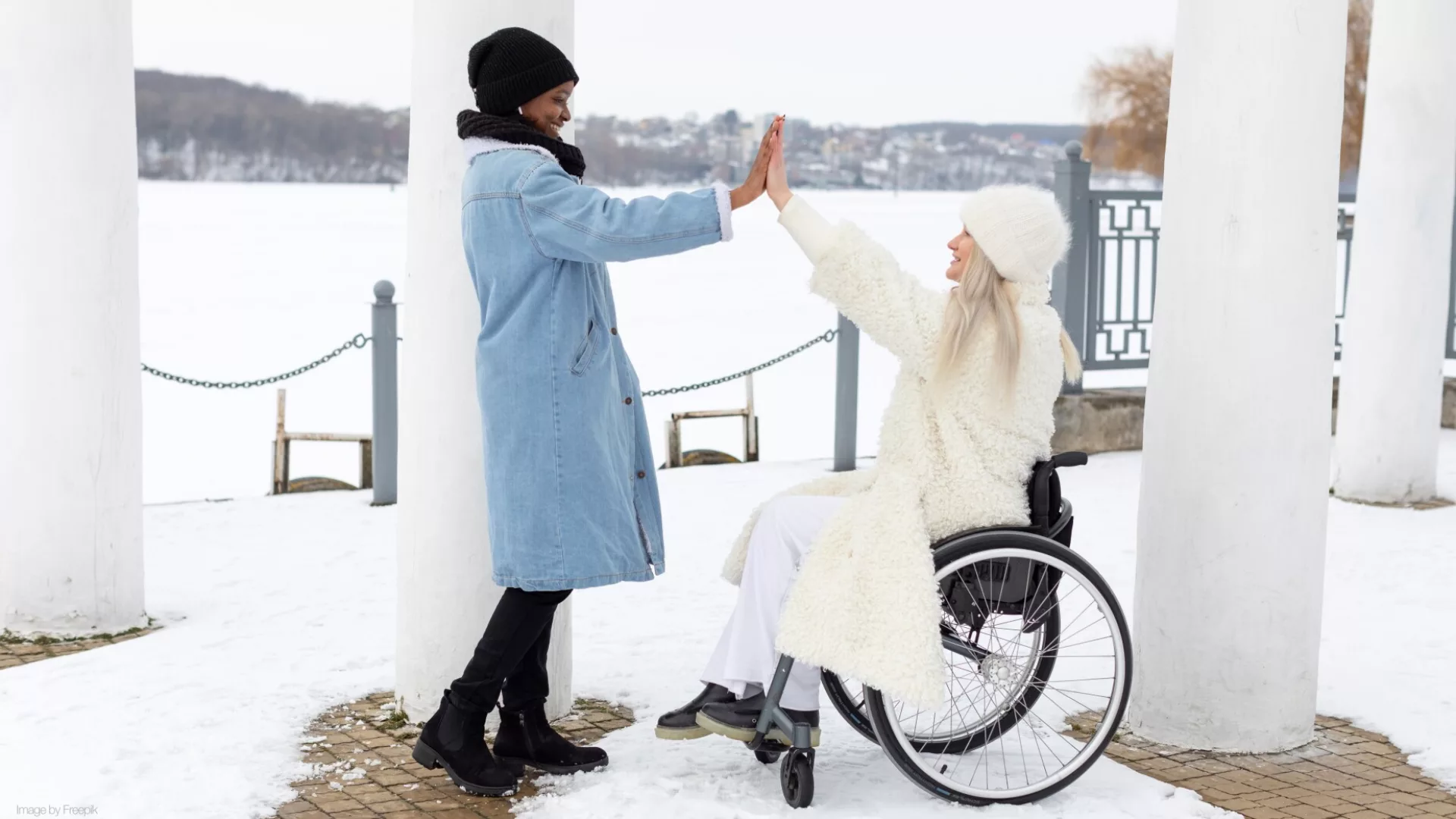 two women high-fiving and smiling at each other bundled up outside in the snow