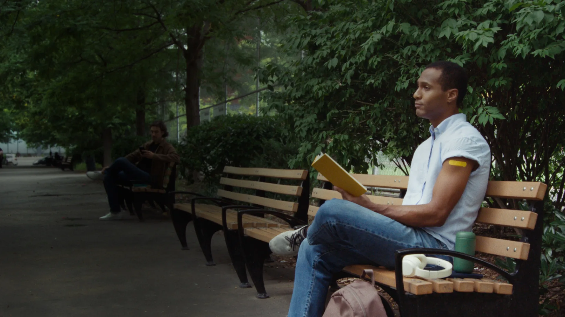 Man reading a book on a bench, bright bandaid on his arm showing his flu shot
